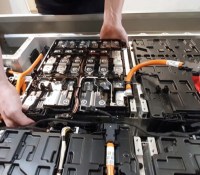 close-up of a mechanic's hands disassembling an electric car battery on top of a trailer inside a mechanic shop