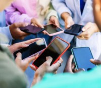 Young group of people standing in circle using mobile phones outside. Unrecognizable teen friends watching social media content on smartphone app. Technology lifestyle concept.